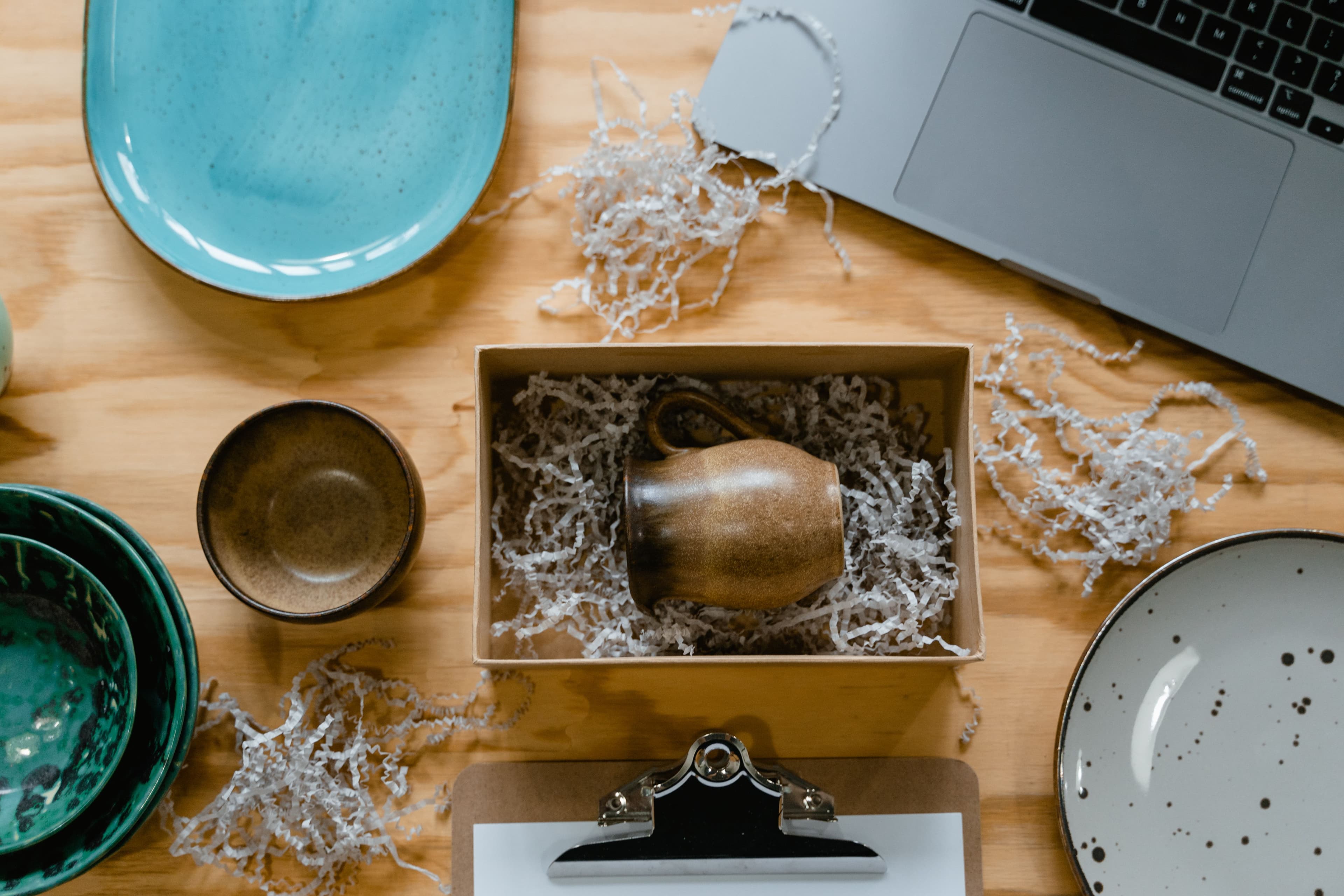 A handmade mug being prepared to be posted in packaging, on a wooden workbench