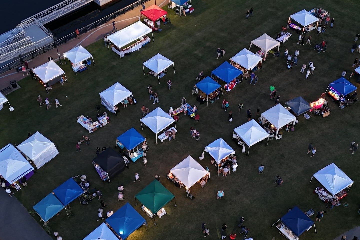 An evening craft market seen from above, rows of gazebos with makers’ stalls set out on the grass