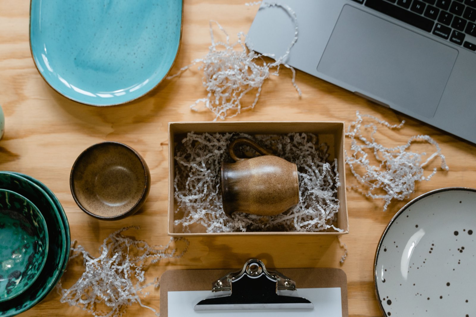 A handmade mug being prepared to be posted in packaging, on a wooden workbench